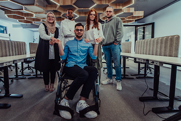 Image showing Young businessmen in a modern office extend a handshake to their business colleague in a wheelchair, showcasing inclusivity, support, and unity in the corporate environment.