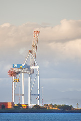 Image showing A crane and shipping containers in a shipyard surrounded by the ocean. Industrial hoisting crane in a logistics or cargo harbor at a seaport for the transportation of liquid materials