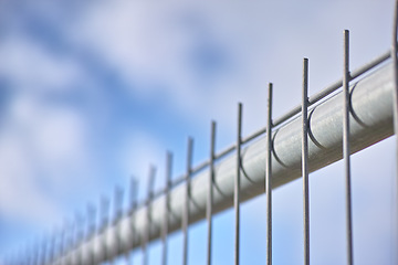 Image showing Closeup of a new metal fence against a cloudy blue sky. Safety and security to protect your home and property. Sharp spikes to keep people out. Constructing a fence or cage. Danger keep out