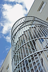 Image showing A spiral staircase on the outside of a building. Grey steel spiral stairs built on the side of modern industrial office building. Low angle of a metal circular fire escape staircase with railings