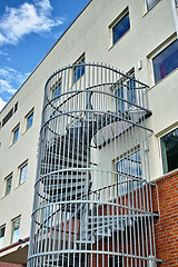 Image showing A spiral staircase running down the side of a building. Emergency exit fire escape. Backyard escape stairs. Caged emergency ladder for the safety of the residents in case of a fire or fire drill