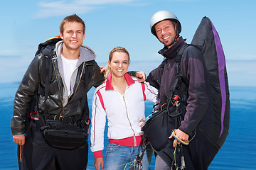 Image showing Men, woman and portrait with happy for paragliding, extreme sport and outdoor by sea in sunshine. Group, fitness and smile on adventure with helmet, backpack or parachute for jump, safety or blue sky