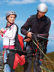 Image showing Man, woman and prepare with safety for paragliding, extreme sport and helping by ocean on mountain. Mentor, fitness and adventure with helmet, backpack and parachute for jump, outdoor and blue sky