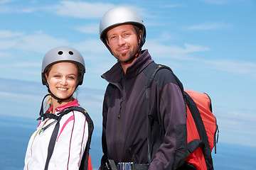 Image showing Man, woman and portrait with smile for paragliding, extreme sport and outdoor by sea in sunshine. Happy couple, fitness and adventure with helmet, backpack or parachute for jump, safety and blue sky