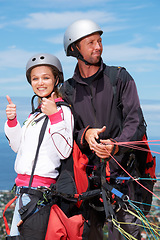 Image showing People, thumbs up and outdoor in nature for paragliding, extreme sport and portrait in sunshine. Man, woman and fitness on adventure with helmet, agreement or parachute with yes, review and blue sky