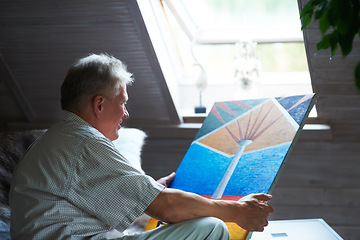 Image showing Senior man, artist or holding painting with pride in home by window for creative art or expression. Picture, painter or mature person in room for watercolor drawing or design on canvas for artwork