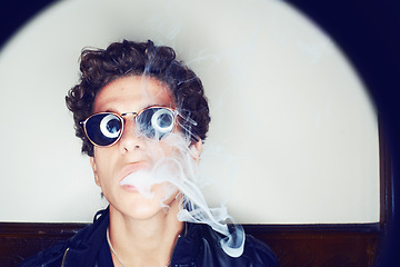 Image showing Portrait of man smoking, sunglasses and grunge fashion with rockstar attitude on white background in spotlight. Cool punk style, creative and smoke, confident face of handsome male model in studio.