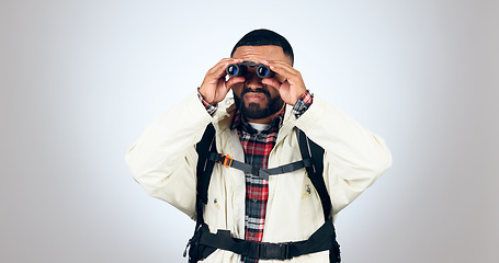 Image showing Man, binoculars and hiking search in studio with backpack for travel and freedom adventure. Camping, watching and grey background and walking with trekking gear for vacation and sightseeing holiday