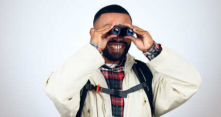 Image showing Man, binoculars and hiking in studio with backpack and smile from travel and freedom with adventure. Camping, happy and grey background and walking with trekking safari gear for vacation and holiday