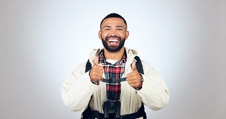 Image showing Man, portrait and thumbs up in studio with backpack and smile from travel freedom with adventure. Camping, fitness and grey background and yes with trekking gear for vacation with hiking motivation