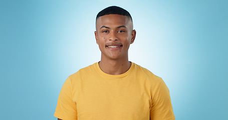 Image showing Happy, smile and portrait of man in a studio with positive, good and confident attitude. Happiness, model and young male person with casual, trendy and cool style with tshirt by blue background.