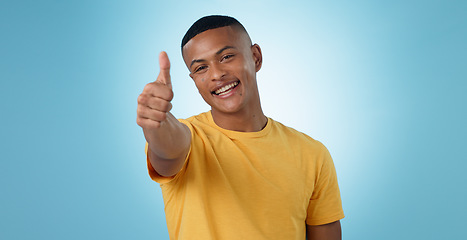 Image showing Thumbs up, portrait and man in studio for agreement, winning deal and celebrate achievement on blue background. Happy model, emoji and like sign for yes feedback, success and thank you for excellence