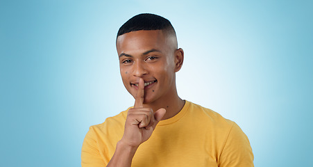Image showing Man, portrait and finger on lips for quiet sign, secret deal or smile in studio for promotion by blue background. Person, hand and cover mouth for icon, emoji or gossip for stop voice, news or drama