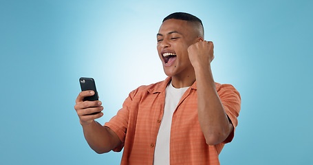 Image showing Man, phone and fist with cheers in studio for trading profit, success or revenue by blue background. Investor, trader or person with smartphone for winning, prize or celebration with online giveaway