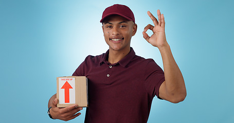 Image showing Delivery man, box and okay hands for success, product excellence and courier services in studio. Happy portrait of supply chain worker or person with package for distribution on a blue background