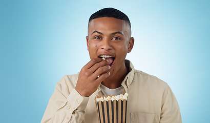 Image showing Portrait, happy man and popcorn for cinema in studio on blue background for entertainment mockup. Male model, eating and hungry with delicious, snack and food for watching, television and theatre