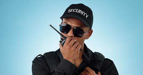 Image showing Security, radio and an officer man on a blue background in studio for surveillance or communication. Face, uniform and sunglasses with a young law person speaking on a walkie talkie for patrol