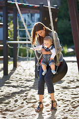 Image showing Mother, baby and swing on park for love, bonding and play with sunshine, child development and care. Woman, kid and infant swinging outdoor in summer for fun, enjoyment and nurture with happiness