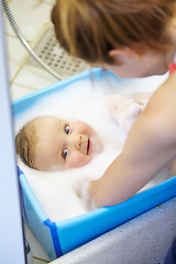 Image showing Baby, mother or smile in bathtub for shower, cleaning and hygiene with foam or bubbles for enjoyment. Child, woman or washing infant in bathroom of home for parenting, development and love with water