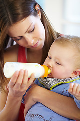 Image showing Mother, baby and holding with bottle in home of formula, feeding or hunger for future growth. Woman, infant or son with nutrition for child development, milestone and health in kitchen with bonding