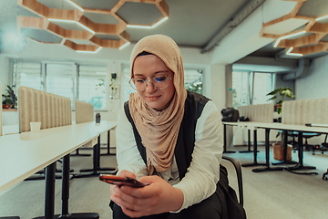 Image showing A businesswoman in a hijab using a smartphone in a modern office, epitomizing a successful and empowered professional in today's tech-savvy world