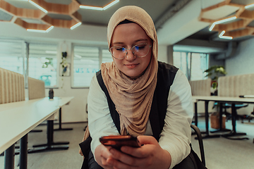 Image showing A businesswoman in a hijab using a smartphone in a modern office, epitomizing a successful and empowered professional in today's tech-savvy world