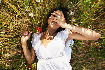 Image showing Woman, flowers and lying outdoor in portrait, peek and smile in spring, vacation or sunshine in nature. Girl, happy and relax with plants, field and hand by eye in countryside with top view in summer