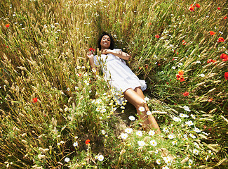 Image showing Woman, flowers and laying in field, portrait and smile in spring, vacation and sunshine in nature. Girl, happy and relax with plants, floral land and outdoor in countryside with top view in summer