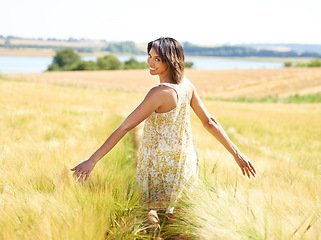 Image showing Back, freedom and portrait of happy woman at field in the countryside outdoor in summer. Rear view, person in nature and open arms at farm, grass and smile on vacation, holiday and travel in Brazil