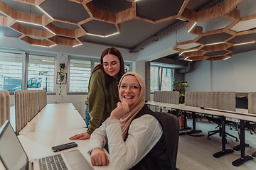Image showing Young businesswomens, one of them wearing a hijab, are collaboratively problem-solving in a modern office while working on a laptop, exemplifying diversity, professionalism, and empowered teamwork