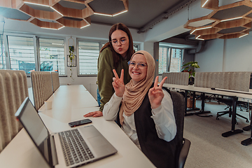 Image showing Young businesswomens, one of them wearing a hijab, are collaboratively problem-solving in a modern office while working on a laptop, exemplifying diversity, professionalism, and empowered teamwork