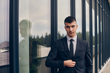 Image showing A CEO dressed in a sleek black suit stands confidently at the entrance of a modern corporate building, awaiting the start of the workday in the bustling urban environment.