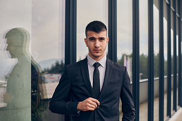 Image showing A CEO dressed in a sleek black suit stands confidently at the entrance of a modern corporate building, awaiting the start of the workday in the bustling urban environment.