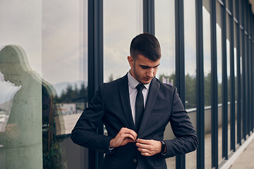 Image showing A CEO dressed in a sleek black suit stands confidently at the entrance of a modern corporate building, awaiting the start of the workday in the bustling urban environment.