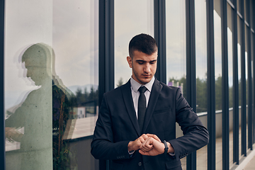 Image showing A CEO dressed in a sleek black suit stands confidently at the entrance of a modern corporate building, awaiting the start of the workday in the bustling urban environment.