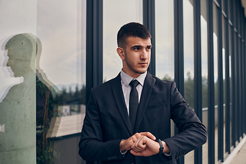 Image showing A CEO dressed in a sleek black suit stands confidently at the entrance of a modern corporate building, awaiting the start of the workday in the bustling urban environment.