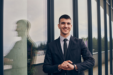 Image showing A CEO dressed in a sleek black suit stands confidently at the entrance of a modern corporate building, awaiting the start of the workday in the bustling urban environment.