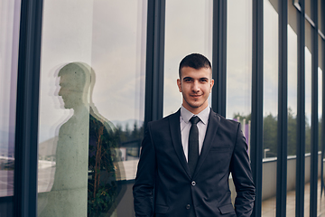 Image showing A CEO dressed in a sleek black suit stands confidently at the entrance of a modern corporate building, awaiting the start of the workday in the bustling urban environment.