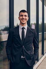 Image showing A CEO dressed in a sleek black suit stands confidently at the entrance of a modern corporate building, awaiting the start of the workday in the bustling urban environment.