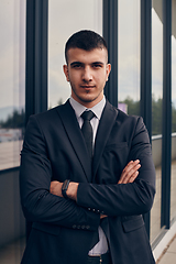 Image showing A CEO dressed in a sleek black suit stands confidently at the entrance of a modern corporate building, awaiting the start of the workday in the bustling urban environment.