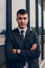 Image showing A CEO dressed in a sleek black suit stands confidently at the entrance of a modern corporate building, awaiting the start of the workday in the bustling urban environment.