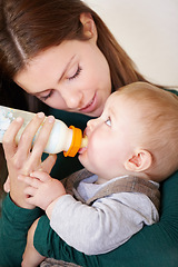 Image showing Woman, holding and baby with bottle for feeding in home for growth, child development or hunger. Mother, son and bond by looking at boy for formula, food or milestone in nutrition, health or diet