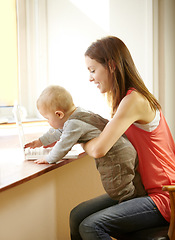 Image showing Mother, holding and baby with laptop in home for remote, work or bond with child in kitchen. Young woman, parenting and son by smile for growth, milestone or development for care, love and support