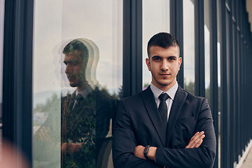 Image showing A CEO dressed in a sleek black suit stands confidently at the entrance of a modern corporate building, awaiting the start of the workday in the bustling urban environment.