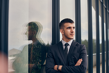 Image showing A CEO dressed in a sleek black suit stands confidently at the entrance of a modern corporate building, awaiting the start of the workday in the bustling urban environment.