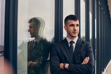 Image showing A CEO dressed in a sleek black suit stands confidently at the entrance of a modern corporate building, awaiting the start of the workday in the bustling urban environment.