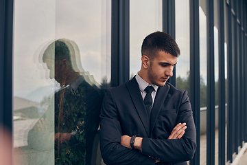 Image showing A CEO dressed in a sleek black suit stands confidently at the entrance of a modern corporate building, awaiting the start of the workday in the bustling urban environment.