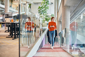 Image showing In a vibrant modern startup office, a businesswoman with striking orange hair is immersed in her work at her desk, embodying the dynamic and creative spirit of contemporary entrepreneurship.