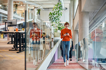 Image showing In a vibrant modern startup office, a businesswoman with striking orange hair is immersed in her work at her desk, embodying the dynamic and creative spirit of contemporary entrepreneurship.