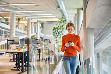 Image showing In a vibrant modern startup office, a businesswoman with striking orange hair is immersed in her work at her desk, embodying the dynamic and creative spirit of contemporary entrepreneurship.